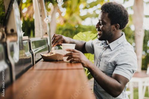 Young african man eating in food truck counter outdoor in city park - Focus on face