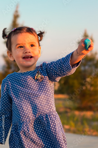 a cute little girl handing a piece of blue chalk outdoors on a sunny day.