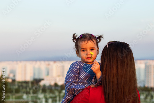 a mother contemplating the cityscape while her daughter smelling a yellow flower with a sad expression on her hands