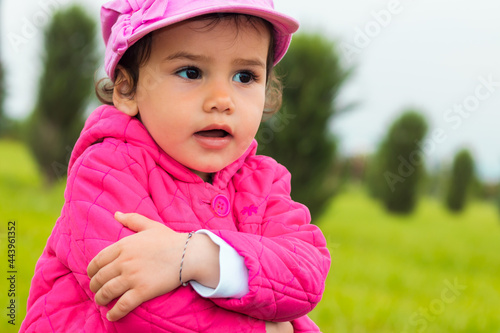 a stubborn 2-year-old girl embracing herself in a park on an overcast day