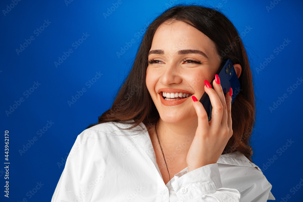 Young brunette woman talking on the phone against blue background Young brunette woman talking on the phone against blue background