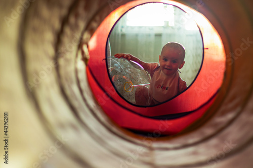 A cute little girl leaning on the transparent air balloon and looking on camera through a colourful tunnel.