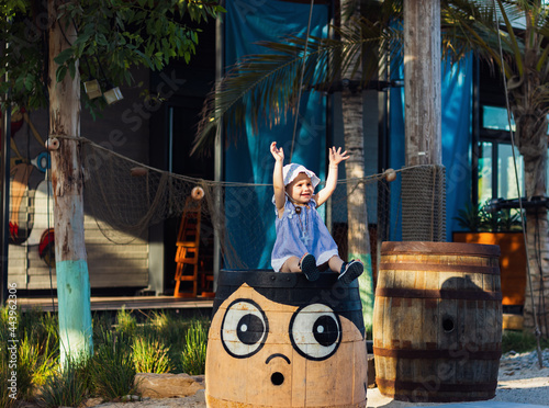 a cute little girl sitting on a wooden barrel in lamer, Dubai on a bright sunny day.
