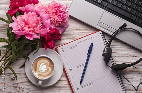 Flat lay women's office desk. Female workspace with laptop, pink peonies bouquet and coffee on white background. Top view feminine background.