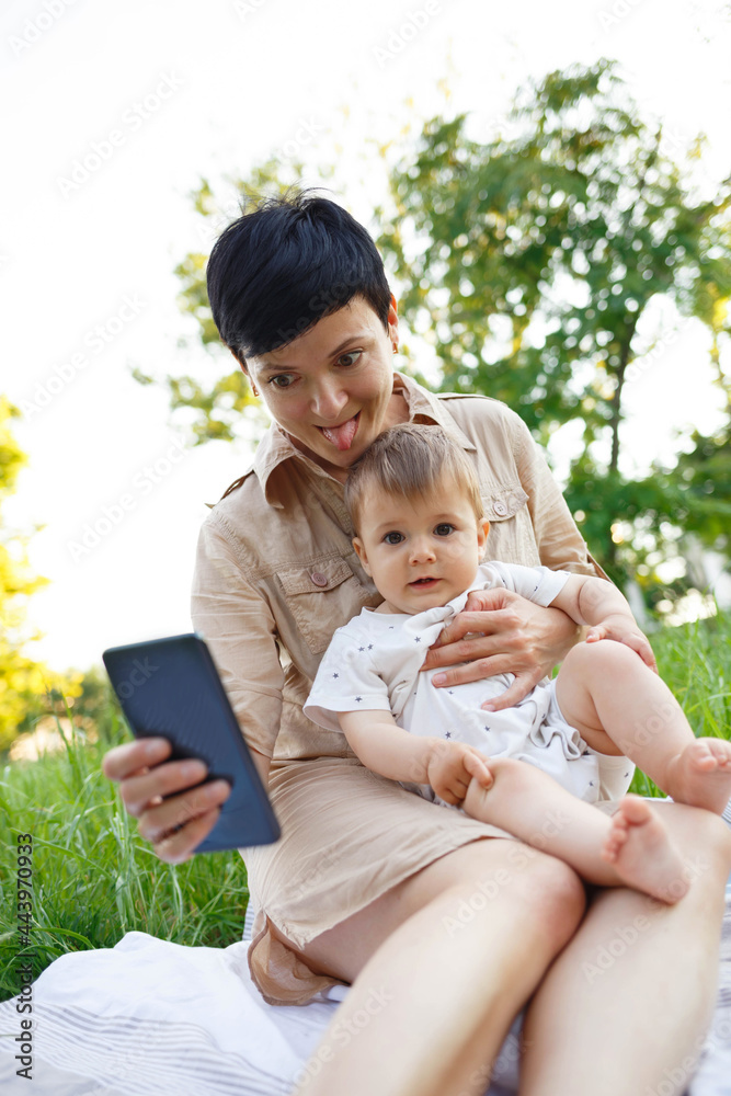 young woman with little son take a selfie while sitting on the green lawn young woman with little son take a selfie while sitting on the green lawn
