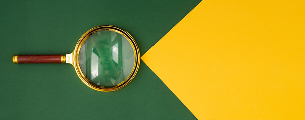 Magnifying lens over green background with yellow paper beam with copyspace for text. Banner with golden loupe.