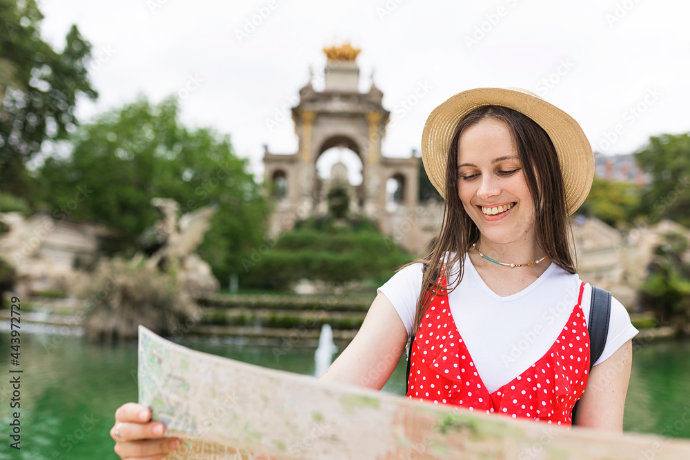 Female tourist checking a map while visiting Ciutadella Park in Barcelona - Cheerful young woman dressed with trendy look traveling alone in an european city during vacation - Summer holidays and