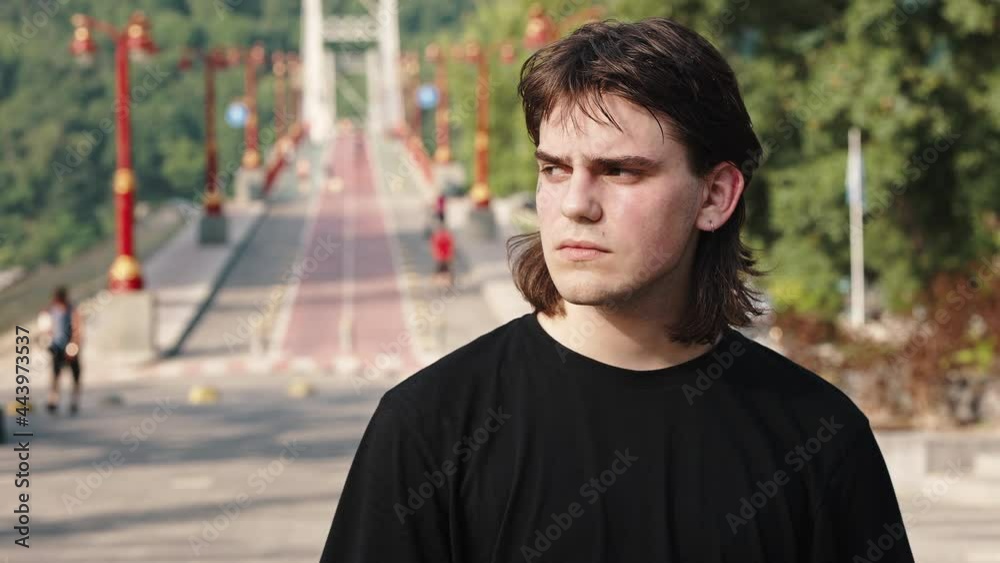 Close portrait of cheerful hipster tattooed guy standing outdoors in urban street looking at camera alone against the background of the bridge. Youth and individual style concept Close portrait of cheerful hipster tattooed guy standing outdoors in urban street looking at camera alone against the background of the bridge. Youth and individual style concept
