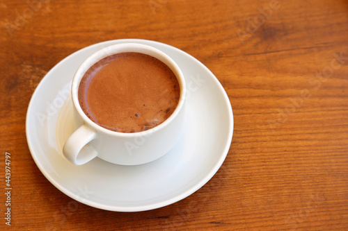 Cup of hot chocolate in a white saucer on wooden table, cocoa drink