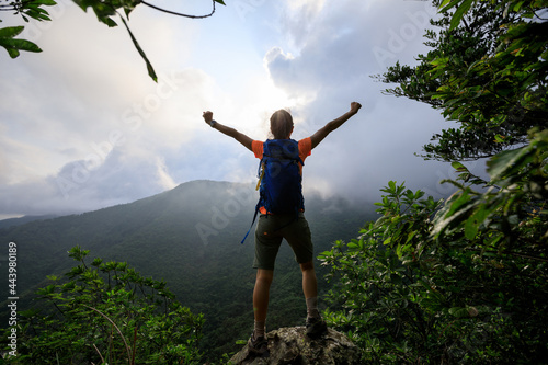 Cheering young woman hiker open arms on mountain peak