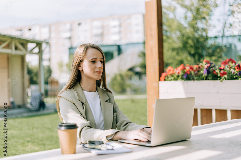 Beautiful blonde business woman working at laptop sit down on bench outside on a urban city street. Happy lady girl in suit distance learning, education and online shopping. Beautiful blonde business woman working at laptop sit down on bench outside on a urban city street. Happy lady girl in suit distance learning, education and online shopping.