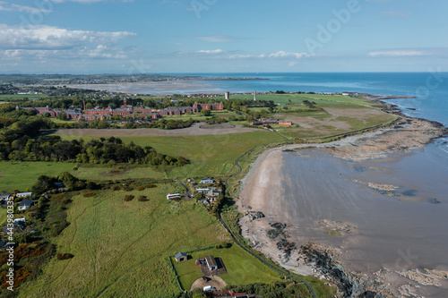 Old brick Quay buildings, the Portrane Round Tower, and Irish landscape.Aerial view of drone flying over rocky beach landscape at Donabate. © Lucian