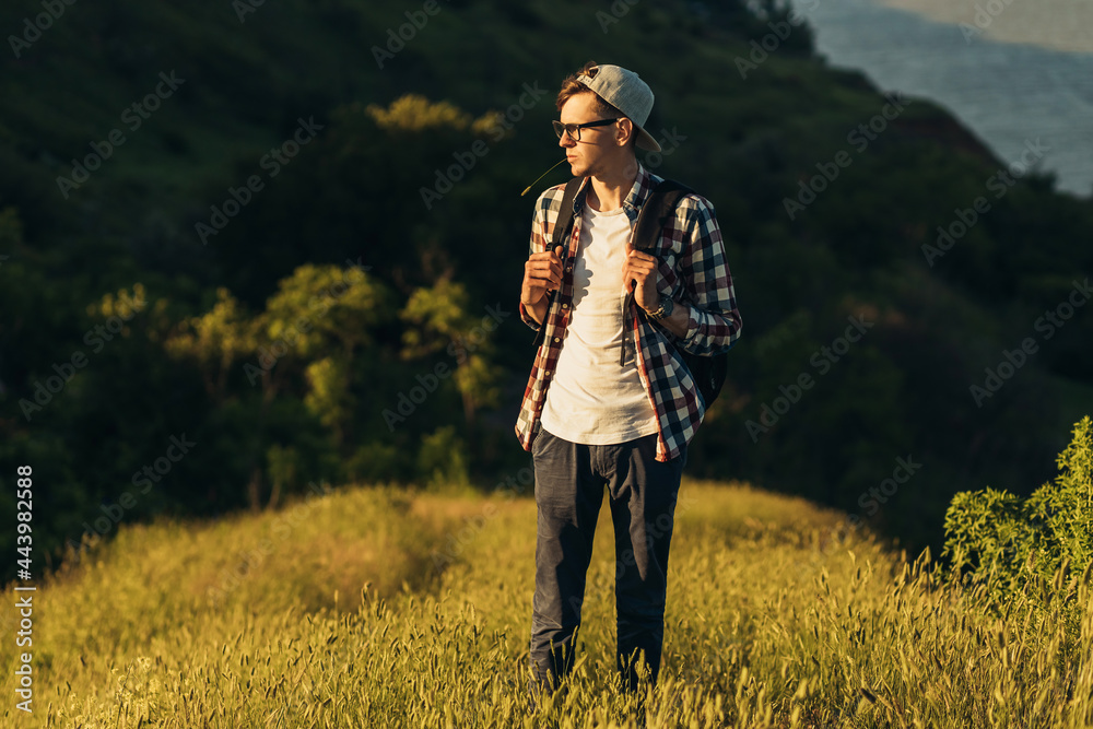 Young traveling man, handsome man in glasses and in a cap, with a backpack, walking in the forests of nature, hiking, active people