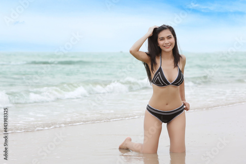 Portrait of young asian beautiful and sexy woman in black bikini sitting on the beach and looking away Cute girl having fun on holiday vacation with happy smiling face. Free space for advertising.