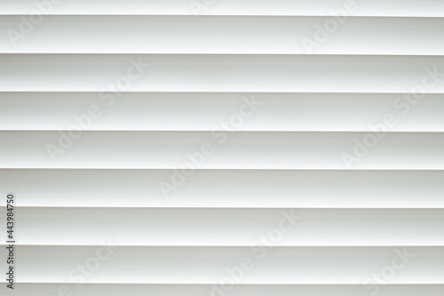 Frontal close-up view of white office shutters made of metal. The curtains cover the window. The strips are horizontally parallel to each other. Texture, background and copy space.