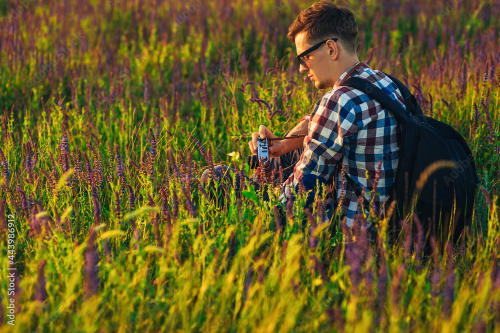 Young male tourist, in sunglasses, with a camera, in nature, spending time in a hike, on the field Young male tourist, in sunglasses, with a camera, in nature, spending time in a hike, on the field