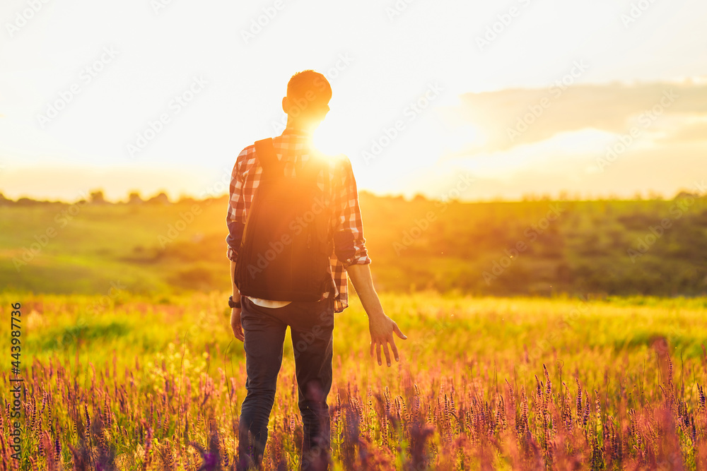 Young man with a backpack, outdoors on the lawn with wildflowers, against the background of zakta, the concept of travel