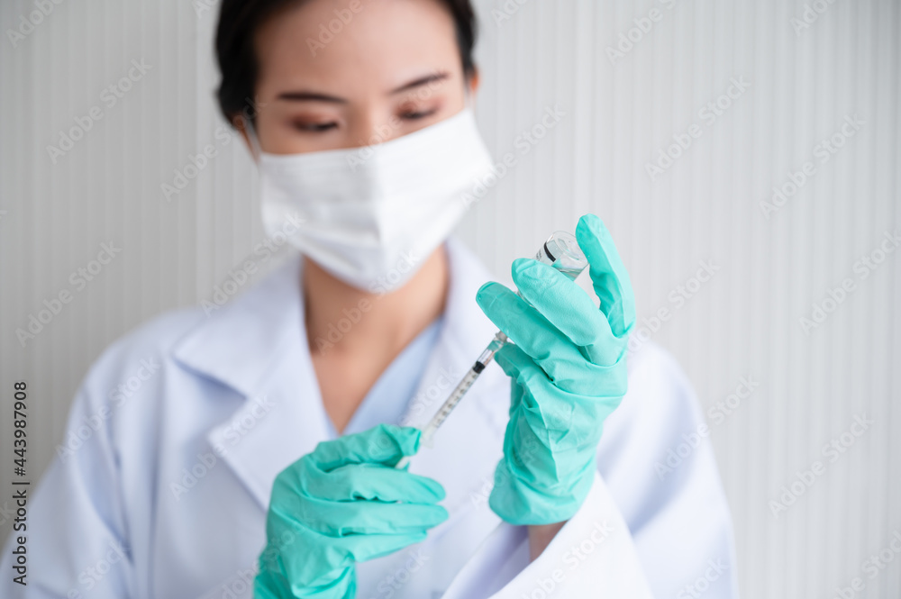 Female doctor wearing gloves and a mask stands holding a syringe with a vaccine. Coronavirus19 in the laboratory. Concept of protection against the COVID-19 virus. Female doctor wearing gloves and a mask stands holding a syringe with a vaccine. Coronavirus19 in the laboratory. Concept of protection against the COVID-19 virus.