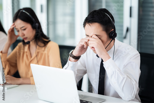 Team of call center staff in Asia wearing headphones with microphones. Stress and headaches while serving customers at desks and computers. Service concept and consulting. communication concept.