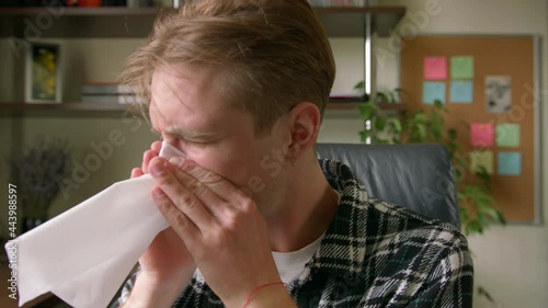 Portrait of sick young man sneezes and blows his nose into a napkin. Close up