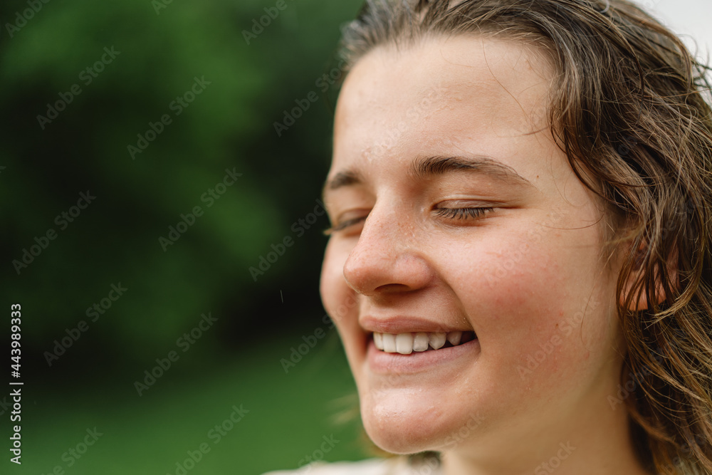Close-Up Portrait Of Teenager Girl. Cheerful Teen Girl With Pronounced Face From Sprayed Small Splashes Of Water Or Warm Summer Rain In Outdoors. Close-Up Portrait Of Teenager Girl. Cheerful Teen Girl With Pronounced Face From Sprayed Small Splashes Of Water Or Warm Summer Rain In Outdoors.