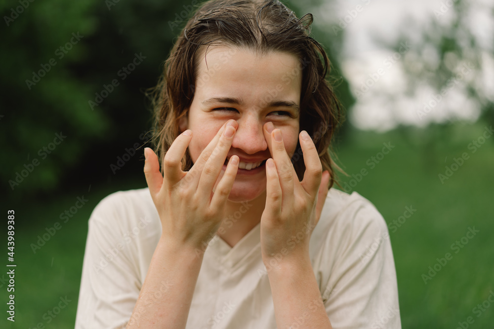 Close-Up Portrait Of Teenager Girl. Cheerful Teen Girl With Pronounced Face From Sprayed Small Splashes Of Water Or Warm Summer Rain In Outdoors. Close-Up Portrait Of Teenager Girl. Cheerful Teen Girl With Pronounced Face From Sprayed Small Splashes Of Water Or Warm Summer Rain In Outdoors.