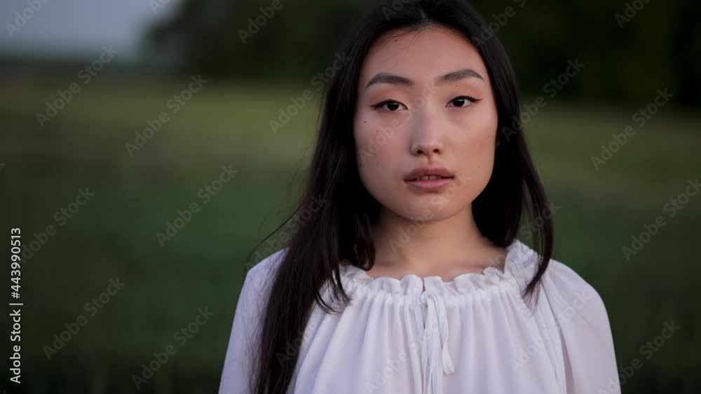 Portrait shot of attractive young asian woman standing in green field. Close up of Womans Face. Portrait of gorgeous girl looking to camera