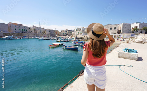 Visit Italy. Rear view of young female tourist holding hat and looking Giovinazzo harbor in Apulia, Italy.