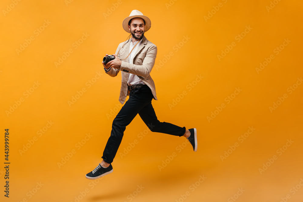 Cool man in dark pants and beige jacket jumps with camera