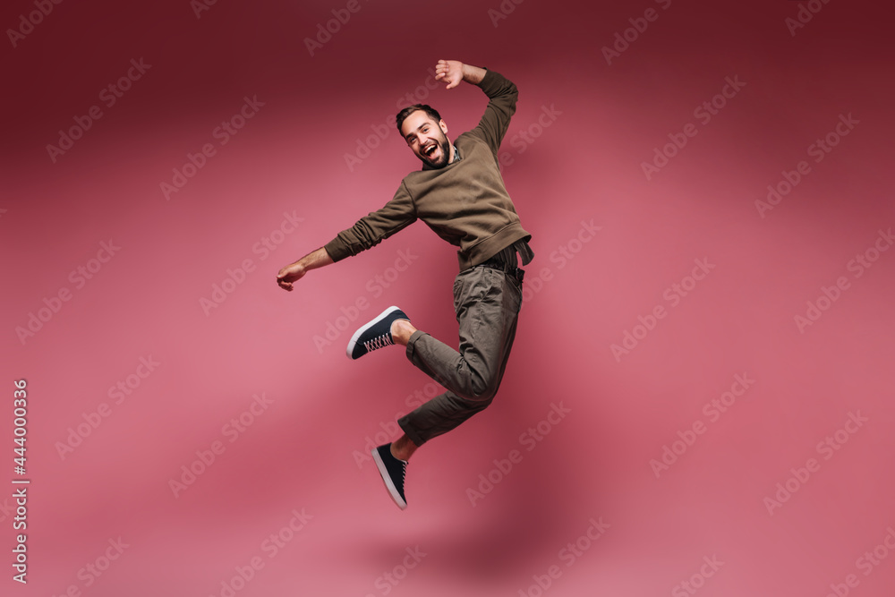 Cheerful man dressed in dark clothes jumping on pink background