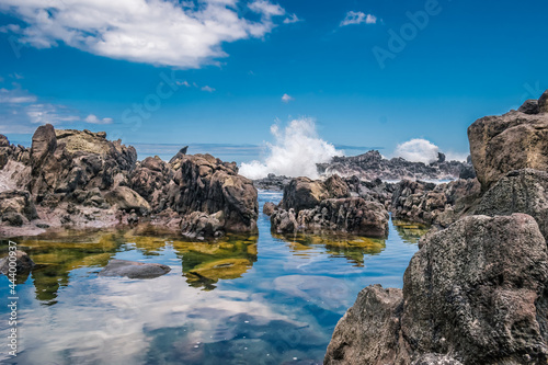 Selective focus in volcanic rocks with crashing waves in the background and clouds reflected in the water, Terceira - Azores PORTUGAL