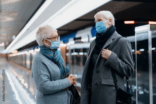 two women in protective masks are talking standing on the subway platform . © yurolaitsalbert