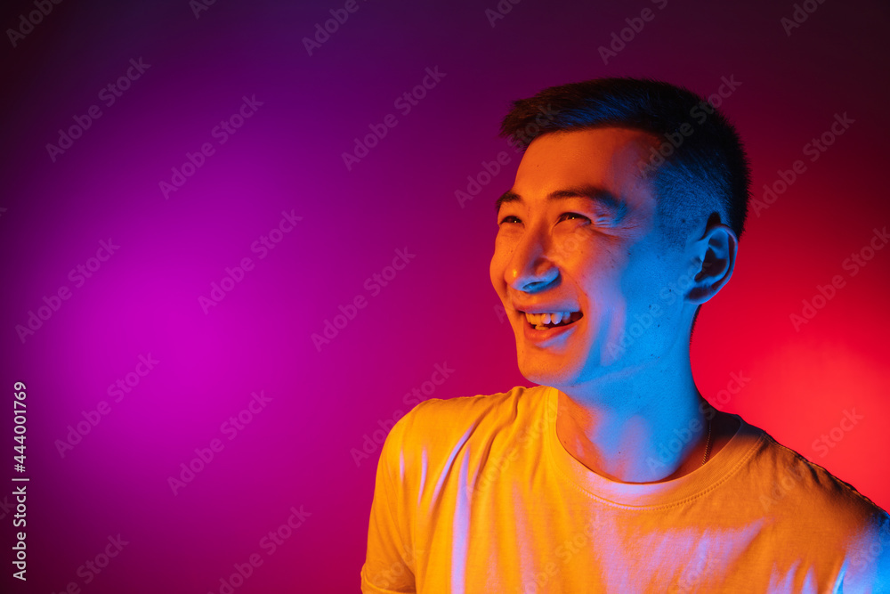 Portrait of Asian young man isolated on studio background in gradient pink purple neon light, colour filter. Concept of human emotions, facial expression. Portrait of Asian young man isolated on studio background in gradient pink purple neon light, colour filter. Concept of human emotions, facial expression.