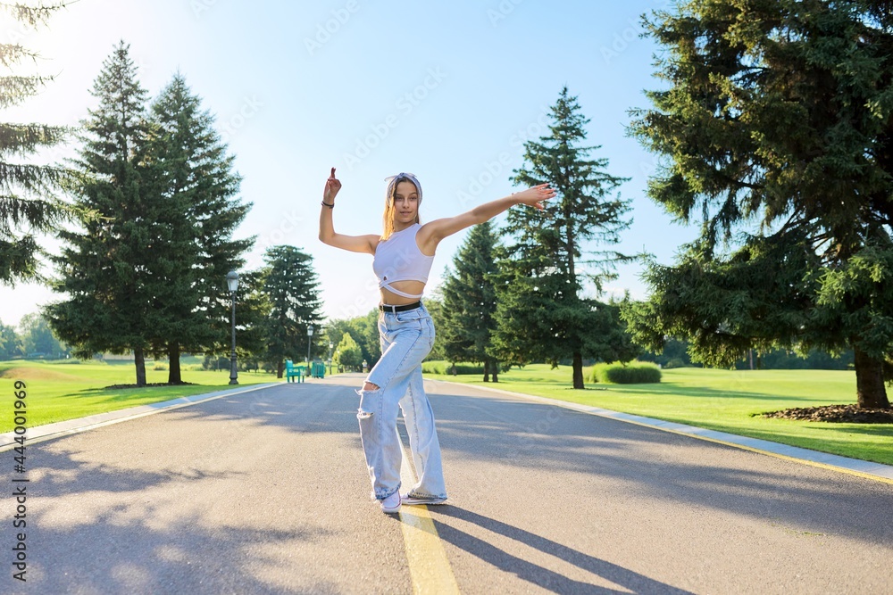 Dancing young female teenager on road in park on sunny summer day