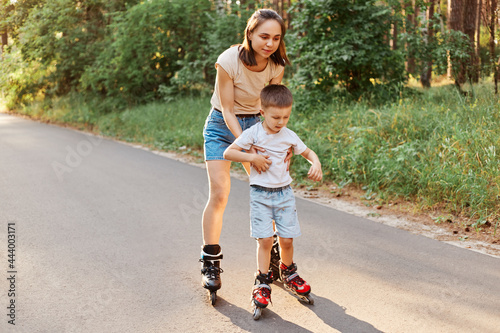 Full length portrait of woman and little son rollerblading together, mother teaching to roller skate his child, cute boy learning riding roller skates. photo