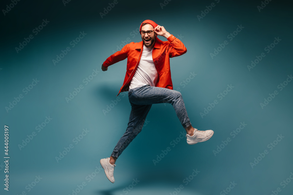 Man in bright outfit holds glasses and jumps on blue background