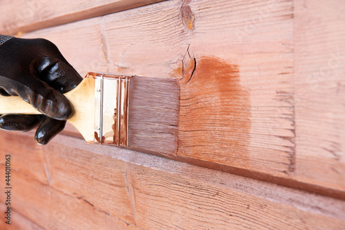Obraz na plátně Man staining log house for protection from weathering
