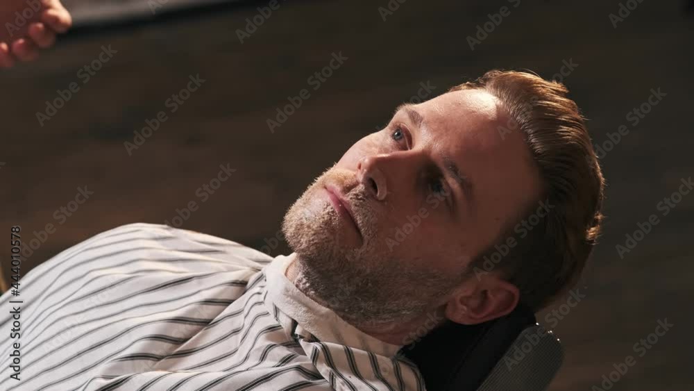 A close-up cropped view of a handsome skillful barber is shaving his client face after haircut with soft brush in barber shop A close-up cropped view of a handsome skillful barber is shaving his client face after haircut with soft brush in barber shop