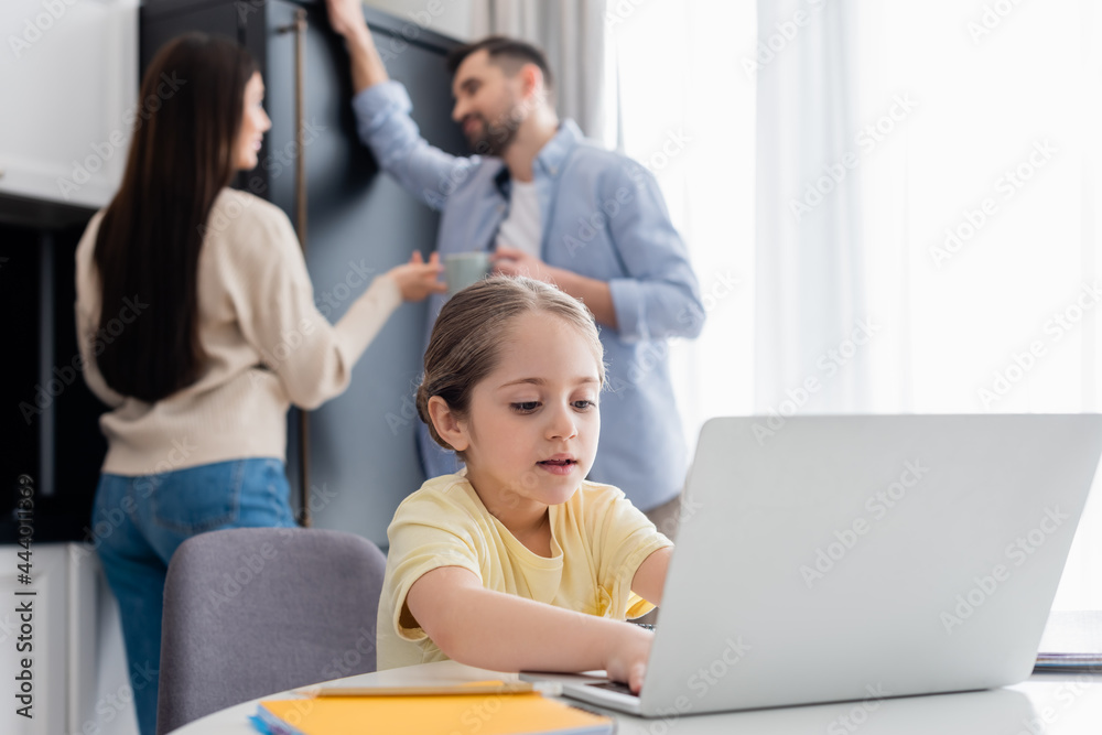 blurred couple talking near child typing on laptop while doing homework blurred couple talking near child typing on laptop while doing homework