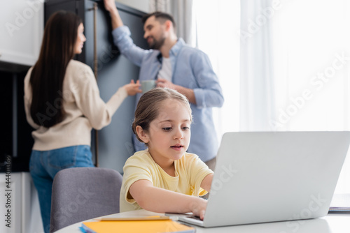 blurred couple talking near child typing on laptop while doing homework © LIGHTFIELD STUDIOS