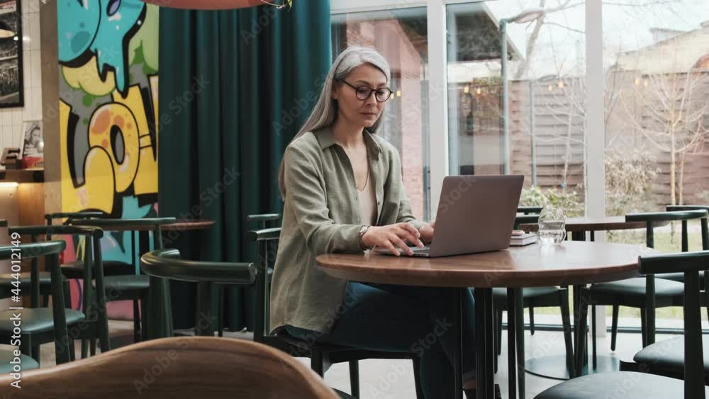 A serious woman wearing eyeglasses using her laptop sitting at the cafe inside A serious woman wearing eyeglasses using her laptop sitting at the cafe inside