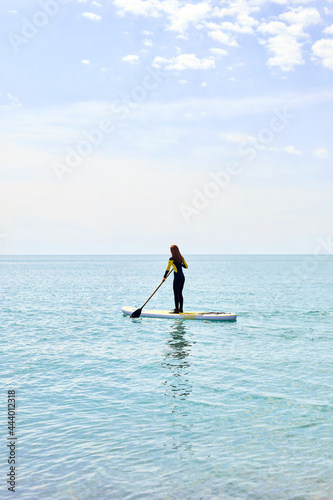 Rear view on woman in black wetsuit with paddle on sub board floats on water in ocean or sea, beautiful caucasian woman engaged in subsurfing alone. Healthy lifestyle concept, water sports. Copy space photo