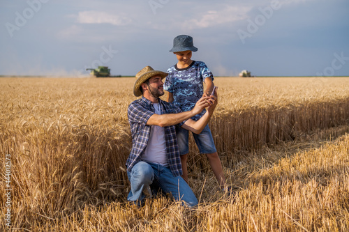 Farmers are standing in their wheat field while the harvesting is taking place. Father is teaching his son about agriculture. © djoronimo