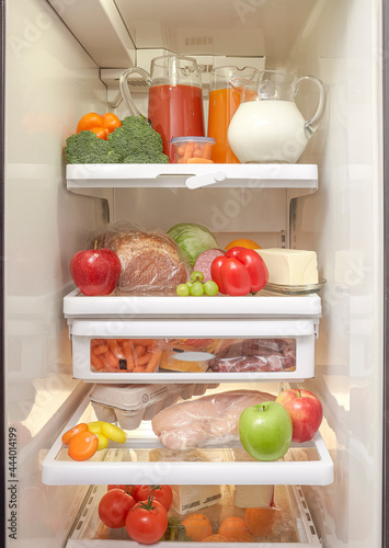 An open refrigerator with healthy fruits  vegetables  and meat 