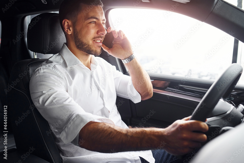 Successful man. Young guy in white shirt is sitting inside of a modern new automobile Successful man. Young guy in white shirt is sitting inside of a modern new automobile