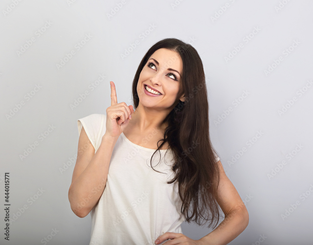 Beautiful excited casual woman pointing the finger up with toothy smiling on empty copy space Beautiful excited casual woman pointing the finger up with toothy smiling on empty copy space