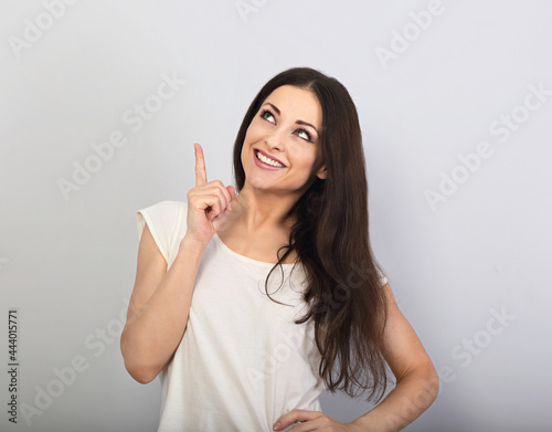 Beautiful excited casual woman pointing the finger up with toothy smiling on empty copy space