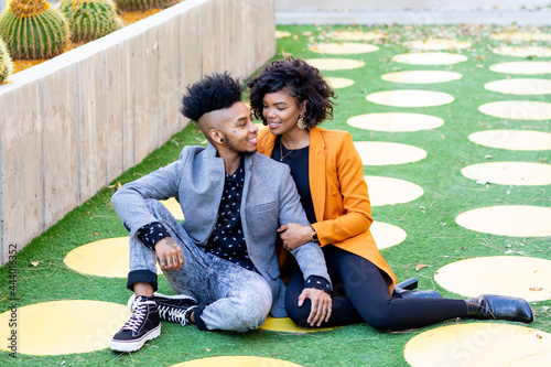 African American transgender couple sitting and smiling at each other on grass photo