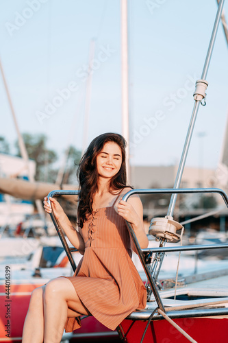 young girl in a dress sits on a boat on a pier on the sea in the summer evening, the setting sun, vacation
