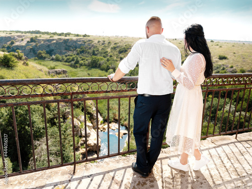 Wedding romantic couple man and woman looking on river, hills, skyline standing on brige at summer sunny day photo